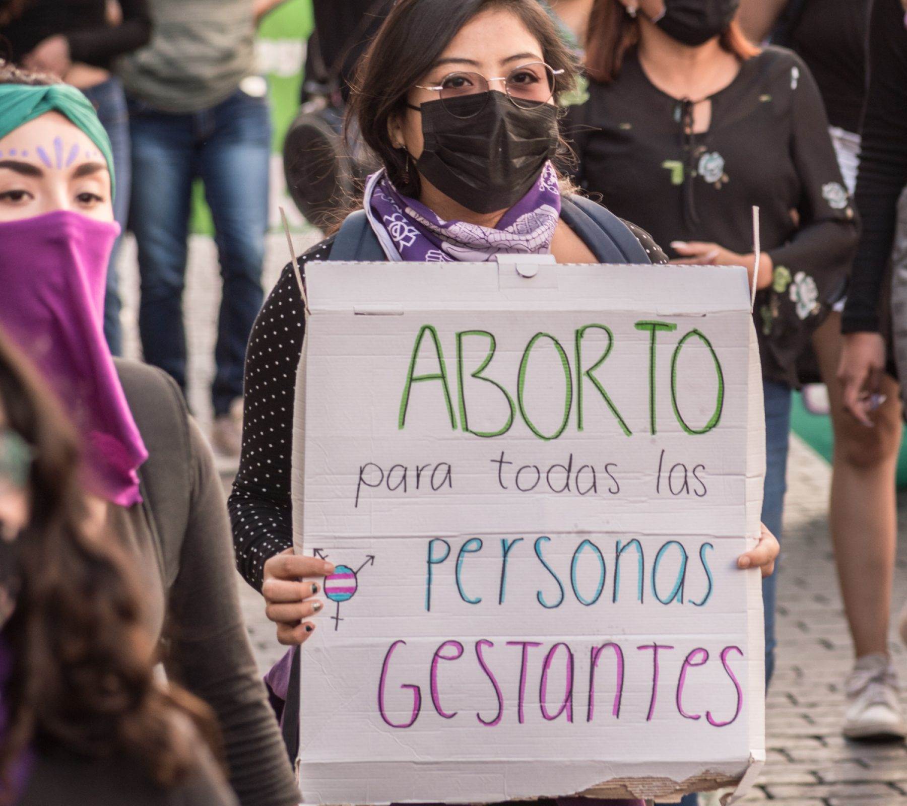 Fotografía de una mujer que carga un cartel que dice aborto para todas las personas gestantes.